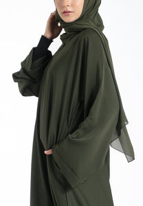 Woman wearing an olive green hijab and abaya on a white background