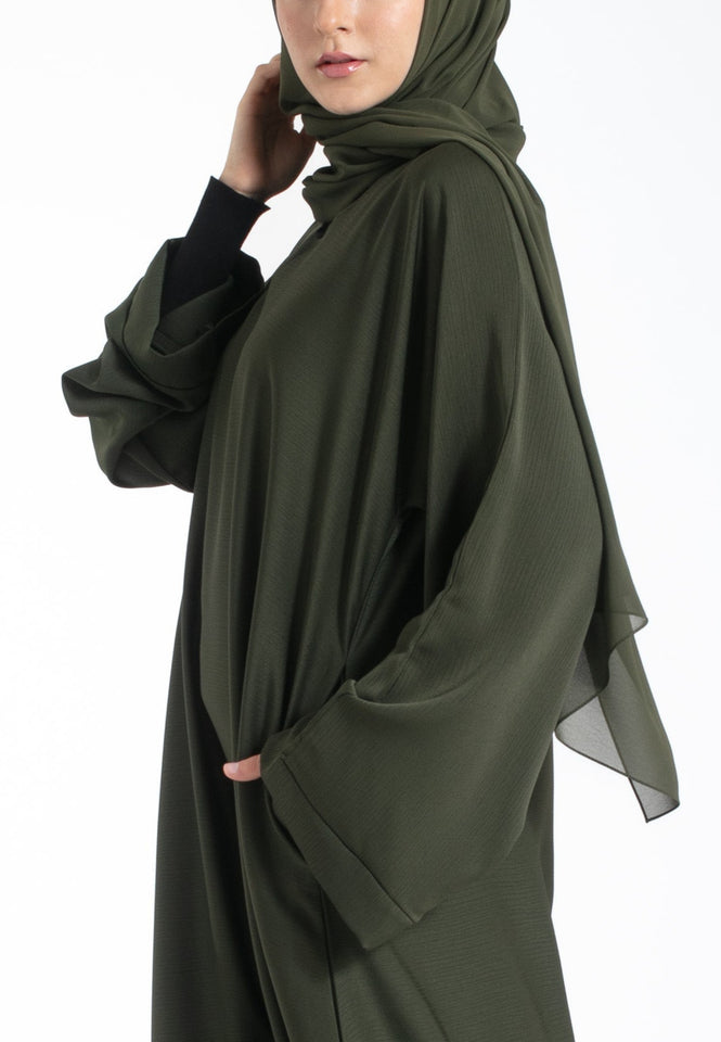 Woman wearing an olive green hijab and abaya on a white background