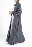 Woman wearing a gray abaya with a white shirt underneath on a white background
