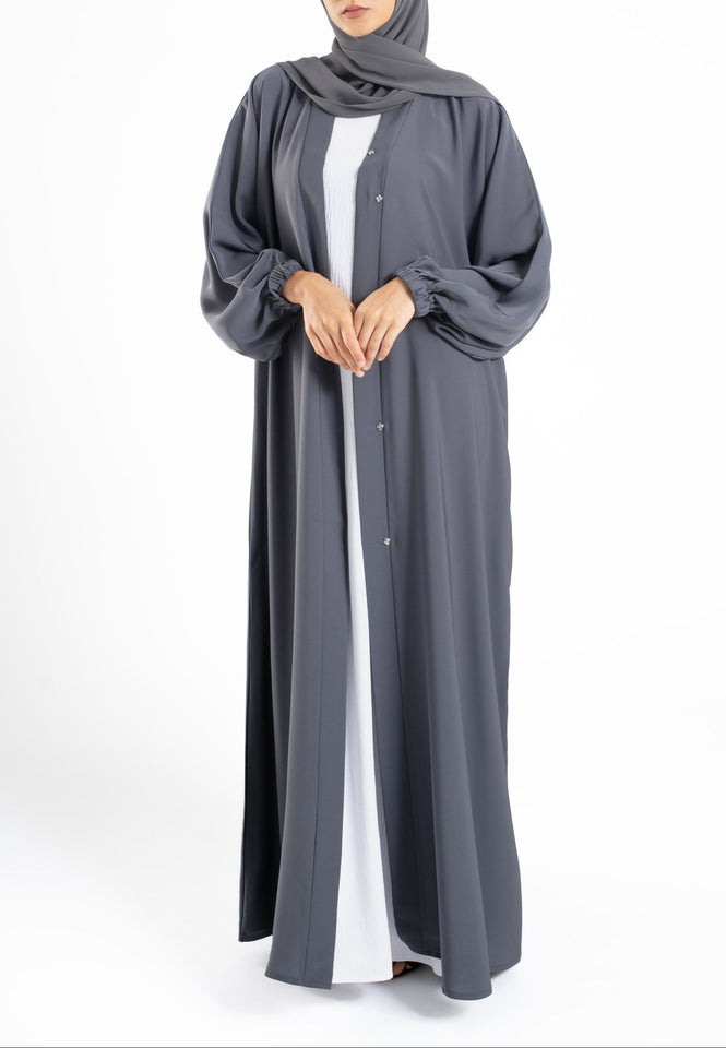 Woman wearing a gray abaya with a white shirt underneath on a white background