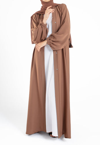 Woman wearing a brown abaya over a white dress on a white background