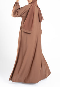 Woman wearing a brown abaya and hijab on a white background