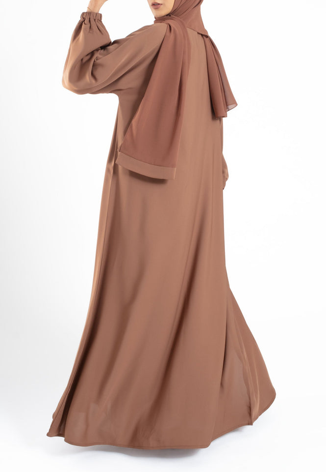 Woman wearing a brown abaya and hijab on a white background