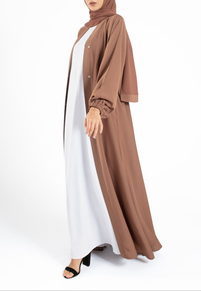 Woman wearing a brown hijab and abaya on a white background