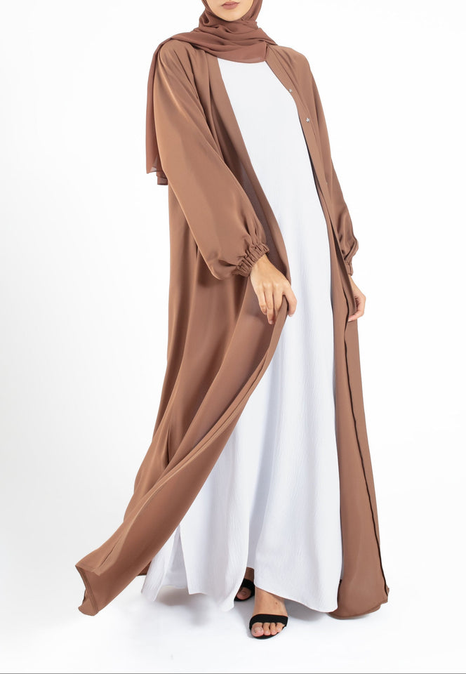 Woman wearing a brown abaya and hijab on a white background